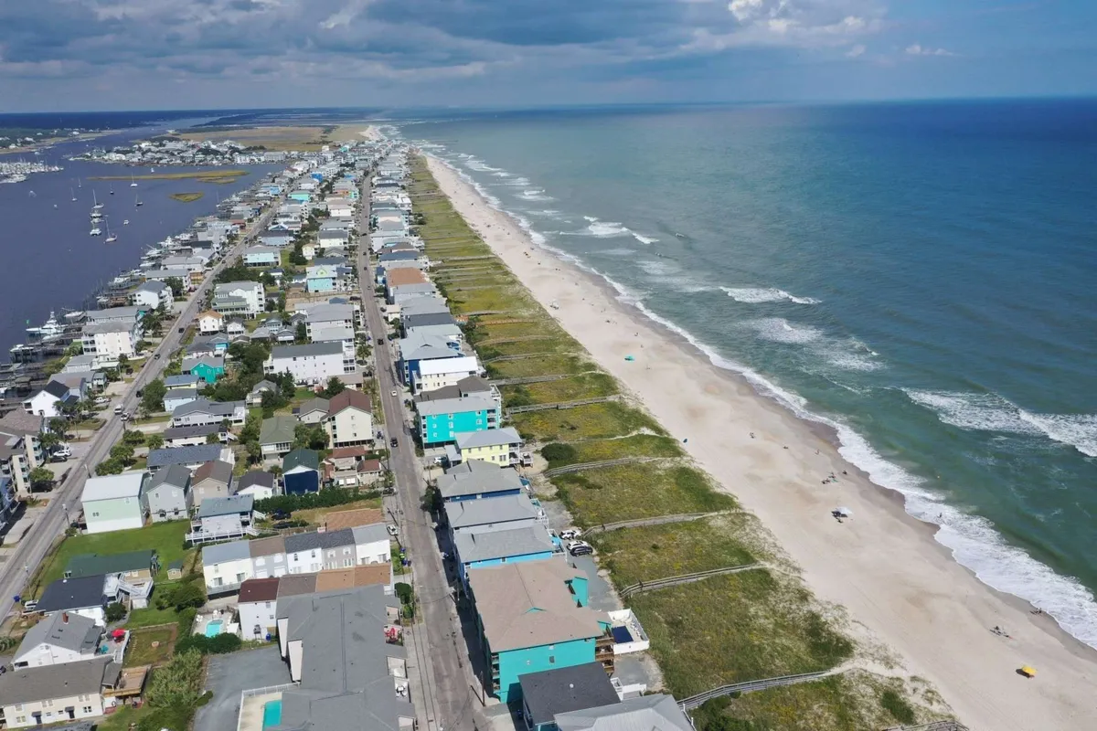 A wide-angle exterior view showcasing beachfront properties right along the sand, with gentle ocean waves and boats visible in the distance. The sandy beach and open waterfront create an inviting atmosphere for outdoor activities and relaxation.