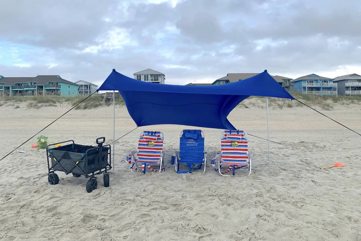 A collection of beach chairs, a blue canopy, and a beach cart are arranged on pale sand with the ocean visible beyond. The scene radiates readiness for a carefree day by the water, with gear prepped and waiting.