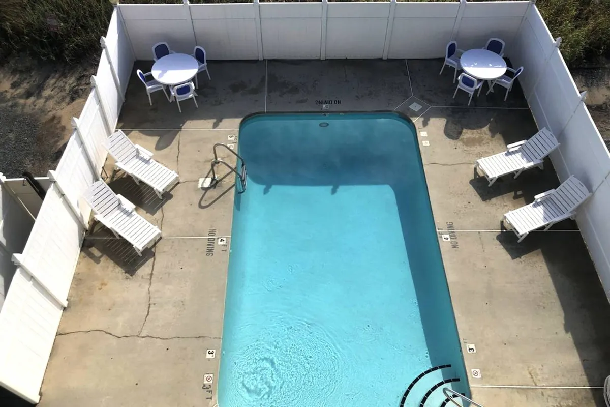 The sparkling community pool is surrounded by lounge chairs and outdoor tables, all bathed in natural light. The pool area looks fresh and inviting, offering a resort-like atmosphere for relaxation or socializing between beach outings.