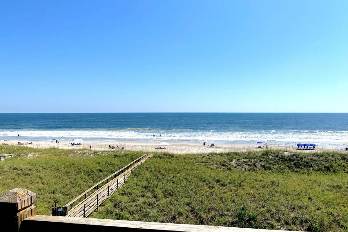 A scenic view with the beach in the foreground, sparkling ocean water, a clear blue sky, and a boardwalk leading out toward the sand. This perspective highlights the inviting nature of the coastline and the ease of accessing the beach.