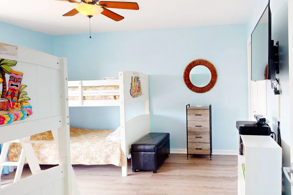 A cheerful bedroom with a colorfully decorated bunk bed, circular mirror, TV, and organized storage unit. The setup is fun, practical, and kid-friendly, with ample space for both sleep and play.